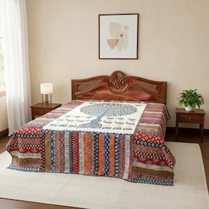 Könnte beinhalten: Eine farbenfrohe Tagesdecke mit einem Lebensbaum-Motiv. Der Quilt zeigt ein zentrales weißes Feld mit einer blauen Baumillustration, umgeben von gemusterten Bordüren in Rot, Blau, Orange und Braun. Die Tagesdecke liegt auf einem hölzernen Bettrahmen.