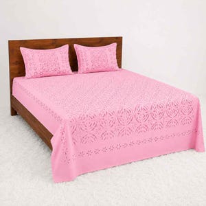 May include: A bright pink bed sheet set featuring two matching rectangular pillowcases and a large bed cover. The fabric displays a repeating laser-cut floral pattern across the surface, creating a delicate, perforated design throughout the bedding.
