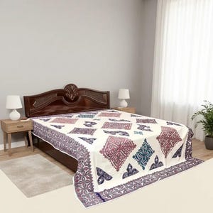 May include: A white bedspread with a geometric pattern in shades of purple, blue, and green. The bedspread is draped over a dark brown wooden bed frame. The room has a neutral color scheme with a gray wall and white curtains.