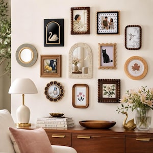 May include: A gallery wall arrangement featuring various wall frames in rectangular, arched, and circular shapes. The collection includes wooden, dark, and light-coloured frames displaying art prints of a swan, cat, flowers, and a leaf, alongside a mirror.
