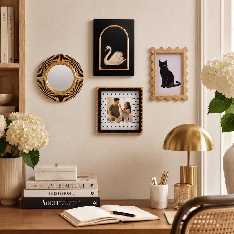 May include: A gallery wall arrangement featuring a round sunburst mirror with a gold center, a black rectangular frame with a gold arch containing a white swan, a scalloped light wood frame with a black cat print, and a square frame with a heart border.