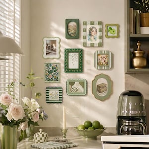 May include: A collection of decorative picture frames in various shapes and sizes, mounted on a wall. The frames are primarily green and white, with a variety of images and artwork inside. A coffee maker and a bowl of limes are on the counter.