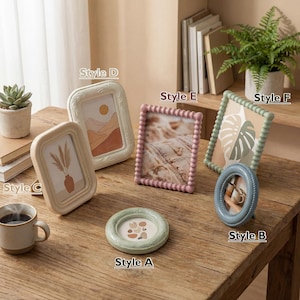 Può includere: Una collezione di cornici decorative per foto in vari stili e colori, tra cui ovali, rettangolari e rotonde. Le cornici sono esposte su un tavolo di legno, mostrando diversi design e dimensioni per l'arredamento della casa.