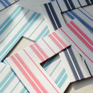 Pode incluir: Close-up de várias molduras com um padrão listrado. As molduras apresentam uma variedade de cores, incluindo listras azul claro, rosa e azul marinho sobre um fundo branco. As molduras estão dispostas em diferentes ângulos.
