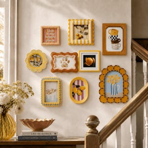 May include: A gallery wall arrangement featuring eight decorative frames in various shapes and sizes, including scalloped, rectangular, and oval designs in shades of yellow, orange, and brown, displaying art prints of lemons, flowers, and text.
