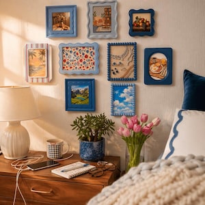 Peut inclure: Une collection de cadres bleus accroch&eacute;s au mur, contenant des images vari&eacute;es : paysages, natures mortes et motifs abstraits. Un chevet avec une lampe, une plante et des accessoires est visible au premier plan.