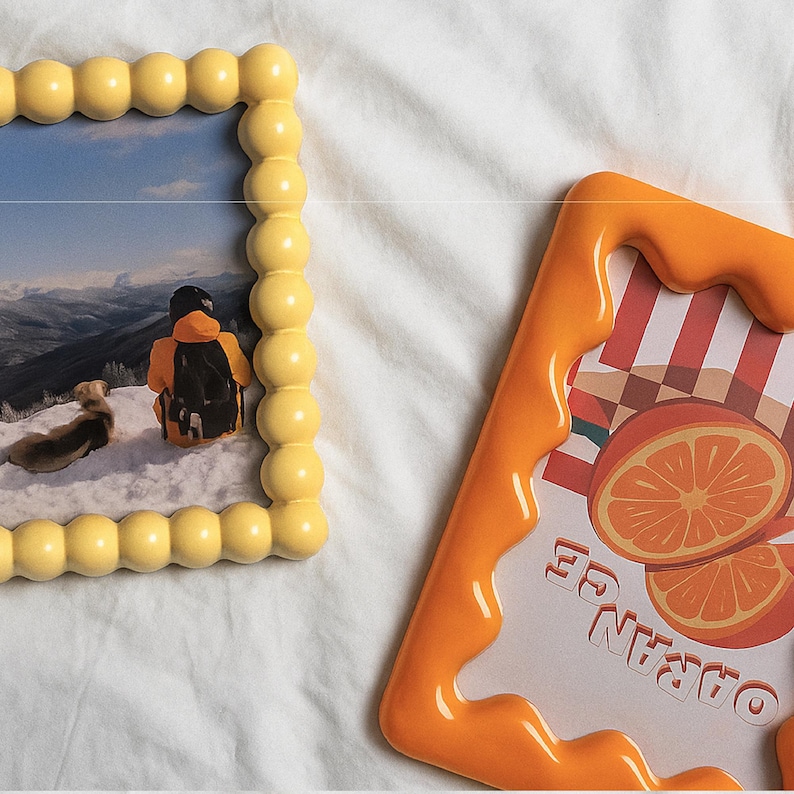 May include: Two decorative picture frames. One is yellow with a bubble design and contains a photo of a person in the snow. The other is orange with a dripping design and features an orange slice graphic with the word "ORANGE".