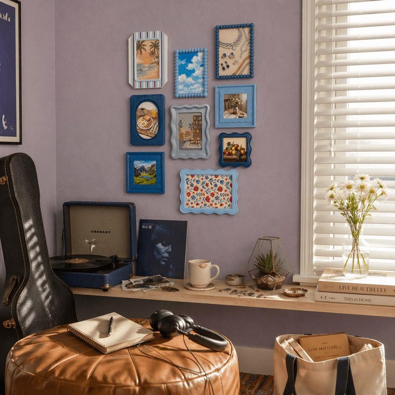 Peut inclure: Une collection de cadres bleus vari&eacute;s, accroch&eacute;s sur un mur lavande. Les cadres pr&eacute;sentent diverses images, notamment des paysages et des motifs floraux. Un tourne-disque vintage, un &eacute;tui de guitare et des objets d&eacute;coratifs compl&egrave;tent la sc&egrave;ne.