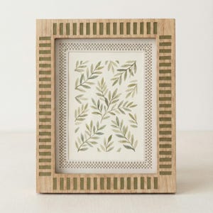 Op de afbeelding: Houten fotolijst met een lichtbruine afwerking en olijfgroene accenten. De lijst omringt een aquarelprint van groene bladeren op een witte achtergrond. De lijst heeft een rechthoekige vorm en een decoratieve rand.