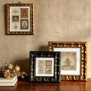 Könnte beinhalten: Drei gerahmte Kunstwerke mit verzierten goldenen und schwarzen Rahmen. Die Rahmen umschließen Vintage-Drucke mit detaillierten Illustrationen. Ein Rahmen hängt an der Wand, während die anderen beiden auf einer Holzoberfläche stehen.
