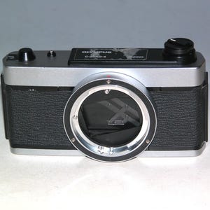 May include: Silver and black Olympus C-35AD-4 camera. The camera has a textured black body, a silver top, and a large lens opening. The top of the camera has a black dial and the Olympus logo.