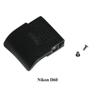 Puede incluir: Puerta de cámara de plástico negro con la palabra "ICARD" impresa en ella. Se incluyen dos pequeños tornillos plateados. Nikon D60.