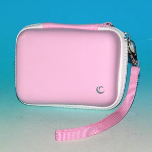 Puede incluir: Estuche rectangular rosa con cremallera, ribete blanco y correa de muñeca rosa a juego. El estuche tiene un pequeño cierre metálico plateado y un logotipo sutil. Diseñado para proteger objetos pequeños.