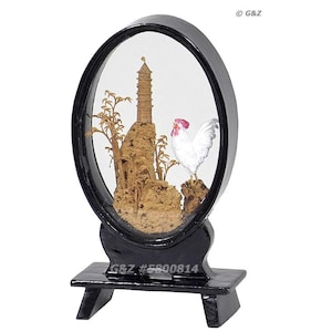 以下が含まれることがあります： 黒いフレームとベースの楕円形のディスプレイケース。内部には、塔、木、白い雄鶏を特徴とするミニチュアの風景があります。ベースには「G&Z #5800814」の文字があります。