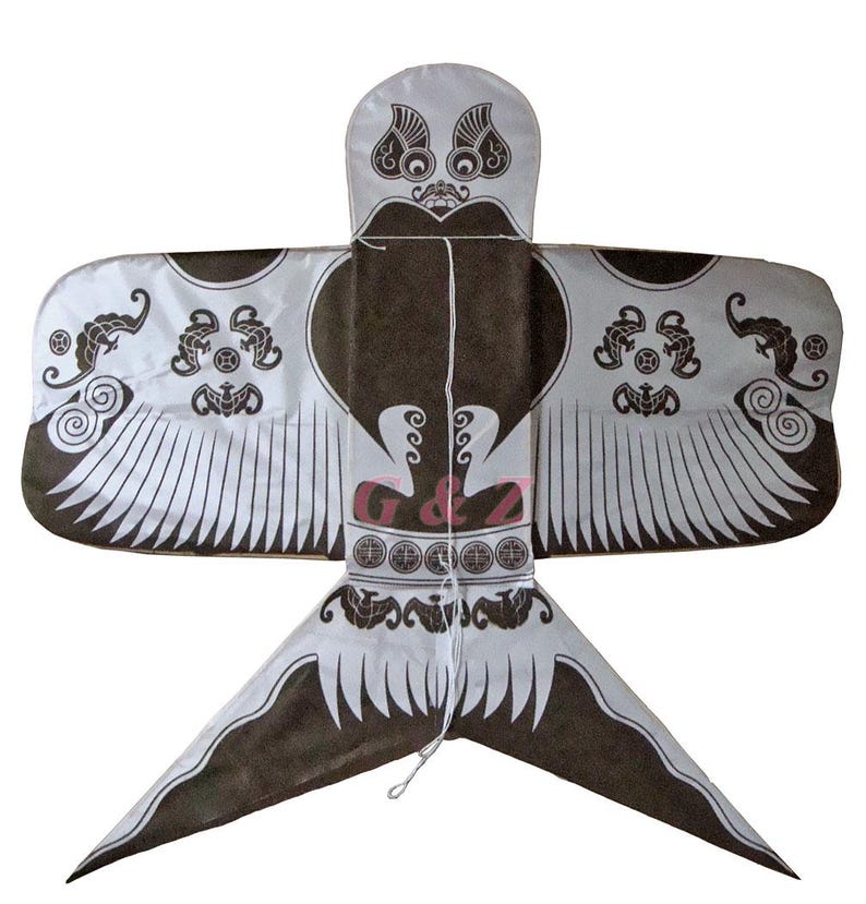 May include: A decorative kite in a bird-like shape, featuring a brown and white color scheme. The kite has a central brown body with white wings and tail, adorned with intricate patterns and designs. The kite has a string attached for flying.