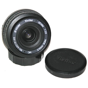 May include: A black Vivitar 28mm 1:2.8 wide-angle camera lens with a 49mm diameter. The lens is accompanied by a black lens cap. The lens has the text "Vivitar" and "WIDE ANGLE" printed on it.