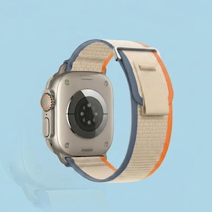 May include: A silver smartwatch with a beige, blue, and orange band. The watch face is square with a black sensor on the back. The band is made of a woven material. The watch is set against a light blue background.