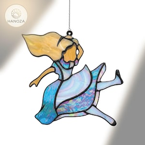 Puede incluir: Vidriera de una figura corriendo con cabello rubio y un vestido azul. La obra de arte está suspendida por una cadena y presenta un diseño colorido e iridiscente. El logotipo "HANOZA" está en la esquina superior izquierda.