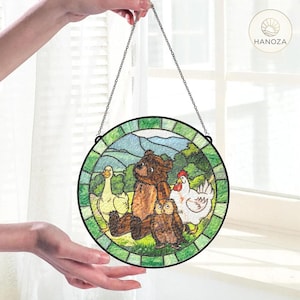 May include: A round stained glass panel featuring a bear, owl, goose, and chicken in a pastoral scene. The artwork is framed with a green border and suspended by a chain. The logo "HANOZA" is visible.