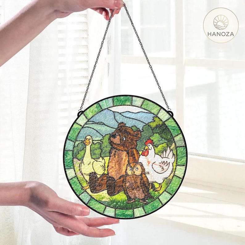 May include: A round stained glass panel featuring a bear, owl, goose, and chicken in a pastoral scene. The artwork is framed with a green border and suspended by a chain. The logo "HANOZA" is visible.