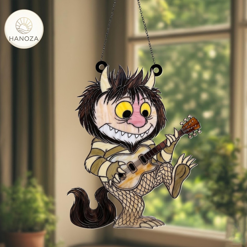 Op de afbeelding: Gebrandschilderde zonnevanger met een cartoonmonster dat gitaar speelt. Het monster heeft bruin haar, gele ogen en een roze neus. Het draagt een gestreept shirt en heeft een lange, donkere staart. De zonnevanger hangt aan een ketting en heeft de merknaam "HANOZA".