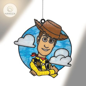 Può includere: Un acchiappasole in vetro colorato raffigurante il personaggio Woody di Toy Story. Woody indossa un cappello da cowboy marrone, una camicia a quadri gialla e un fazzoletto rosso, su uno sfondo di cielo blu con nuvole bianche. L'acchiappasole è progettato per essere appeso.