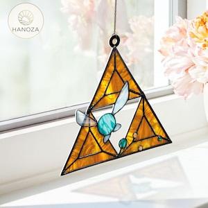 May include: Stained glass suncatcher in a triangular shape with a yellow and orange color scheme. The design includes a blue and green stylized bird. The suncatcher is hanging in front of a window.
