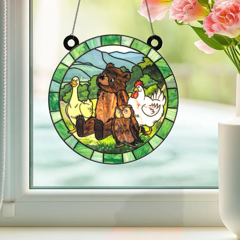 May include: Round stained glass window art featuring a bear, owl, duck, and chicken in a green and blue landscape. The artwork is suspended by a black chain and rings. The design has a cartoonish style.