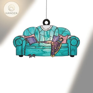 May include: A teal stained glass sofa with purple and pink cushions, a child under a star-patterned blanket, and two small bear figures. The piece is suspended by a chain and ring, with the brand name "HANOZA" visible.
