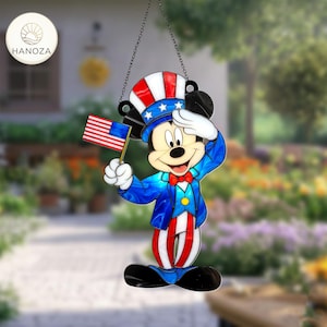 Könnte beinhalten: Eine patriotische Mickey Mouse-Dekoration in Rot, Weiß und Blau, die salutiert und eine kleine amerikanische Flagge hält. Die Figur trägt einen Zylinder mit Sternen und Streifen, eine blaue Jacke und rot-weiß gestreifte Hosen. Die Dekoration hängt an einer Kette.