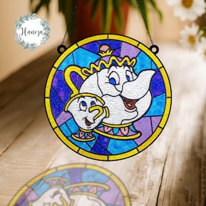 May include: A round stained glass window featuring a cartoon teapot and teacup design. The window has a yellow border and a black chain for hanging. The design includes blue, purple, and white colors.