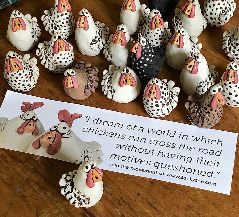 May include: A collection of hand-painted ceramic chickens with black and white polka dots, brown and white, and black and white patterns. The chickens are arranged on a wooden surface with a sign that reads "I dream of a world in which chickens can cross the road without having their motives questioned." Join the movement at www.Beckyzee.com