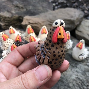 May include: A brown and black speckled ceramic chicken figurine with red and yellow accents. The chicken has large, round eyes and a wide, open beak. The figurine is about 3 inches tall and is standing on a small, flat base.