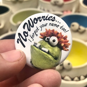 May include: A white button with a green monster with red hair and the text "No Worries... I forgot your name too!"
