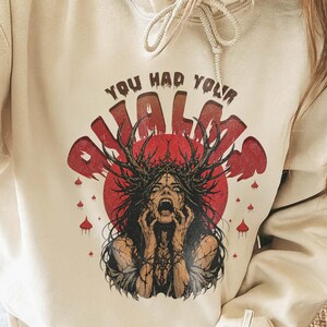 Op de afbeelding: Een crèmekleurige hoodie met een grafische print van een figuur met donker haar en een gewei tegen een rode cirkelvormige achtergrond. De tekst "YOU HAD YOUR CHANCE" staat in een donker lettertype boven de illustratie gedrukt.