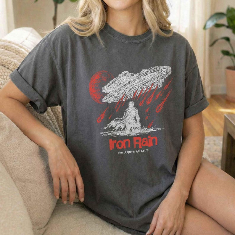 Op de afbeelding: Donkergrijs t-shirt met een wit ruimteschipontwerp en een rode maan. De tekst "Iron Rain" is rood, met de Latijnse zin "Per Aspera Ad Astra" eronder.