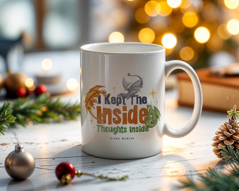 May include: White ceramic mug with a curved handle. The mug features a design with three dragons in orange, gray, and green, along with the text "I Kept The Inside Thoughts Inside". The mug is on a white wooden surface with Christmas decorations.