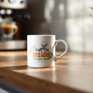 May include: White ceramic mug with the text "I Kept The Inside Thoughts Inside" in a stylized font. The mug features a dragon graphic and other decorative elements. The mug is on a wooden surface.