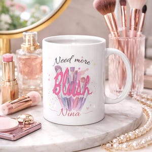 Könnte beinhalten: Eine weiße Keramik-Tasse mit schwarzem Henkel und dem Text "But First, Coffee" in schwarzer, fetter Schrift. Die Tasse steht auf einer weißen Oberfläche. Die Tasse ist etwa 10 cm hoch.