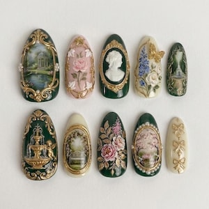 May include: A collection of ten intricately designed artificial nails. Each nail features a different miniature painting or relief design, including landscapes, floral patterns, and cameo portraits, with gold and pearl accents. The nails are in various shades of green, pink, and cream.