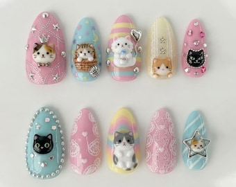 May include: A set of ten artificial nails, each with a unique design featuring cat-themed embellishments. Colors include pink, blue, yellow, and white, with glitter, stars, and heart accents. The nails showcase various cat figurines and patterns.