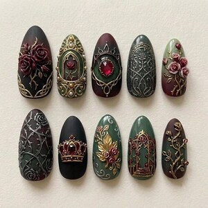 May include: A set of ten almond-shaped press-on nails featuring intricate 3D designs in shades of deep red, forest green, black, and gold. Embellishments include sculpted roses, ornate metal-style filigree, a central red gem, and a crown motif.