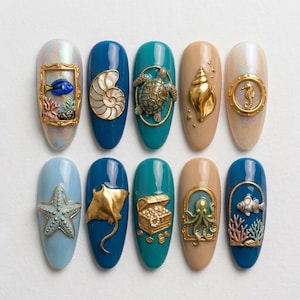 May include: Ten artificial nail tips featuring ocean-themed 3D decorations. Designs include a blue fish in a gold frame, a nautilus shell, a sea turtle, a gold conch, a seahorse in a porthole, a starfish, a stingray, a treasure chest, an octopus, and a fish.