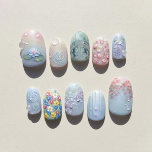 May include: A set of ten artificial nails with various designs. The designs include a water lily, a bridge over water, floral patterns, and water droplet accents. The nails are painted in pastel colors, including pink, blue, and white.
