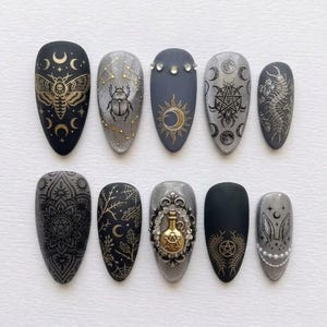 May include: A set of ten almond-shaped press-on nails featuring matte black and metallic silver finishes. Designs include gold moth, scarab, sun, moon, pentagram, centipede, mandala, spiderweb, rabbit, and potion bottle motifs with rhinestones.