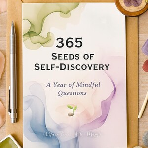 May include: A journal titled "365 Seeds of Self-Discovery" with the subtitle "A Year of Mindful Questions." The cover features watercolor-style artwork in shades of green, blue, and purple. A silver pen and a watercolor palette are also visible.