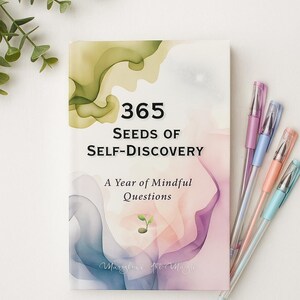 May include: A book titled "365 Seeds of Self-Discovery" with the subtitle "A Year of Mindful Questions." The cover features watercolor-style art in shades of green, pink, and purple. Several pastel-colored pens are arranged beside the book.