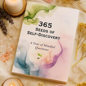 May include: A book titled "365 Seeds of Self-Discovery" with a watercolor design. The cover features green, blue, and purple hues. The book is surrounded by candles, crystals, and dried flowers, creating a serene aesthetic.