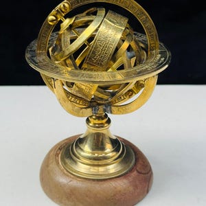 Könnte beinhalten: Eine Messing-Armillarsphäre auf einem Holzsockel. Die Sphäre hat mehrere Ringe mit eingravierten Markierungen und einen zentralen Globus. Der Sockel ist dunkelbraun. Es ist ein dekorativer Gegenstand.