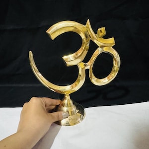 Peut inclure: Une sculpture dorée du symbole Om. Le symbole Om est un son sacré et une icône spirituelle dans l'hindouisme, le bouddhisme et le jaïnisme. La sculpture est en métal et a une finition polie. La sculpture est sur une base ronde.